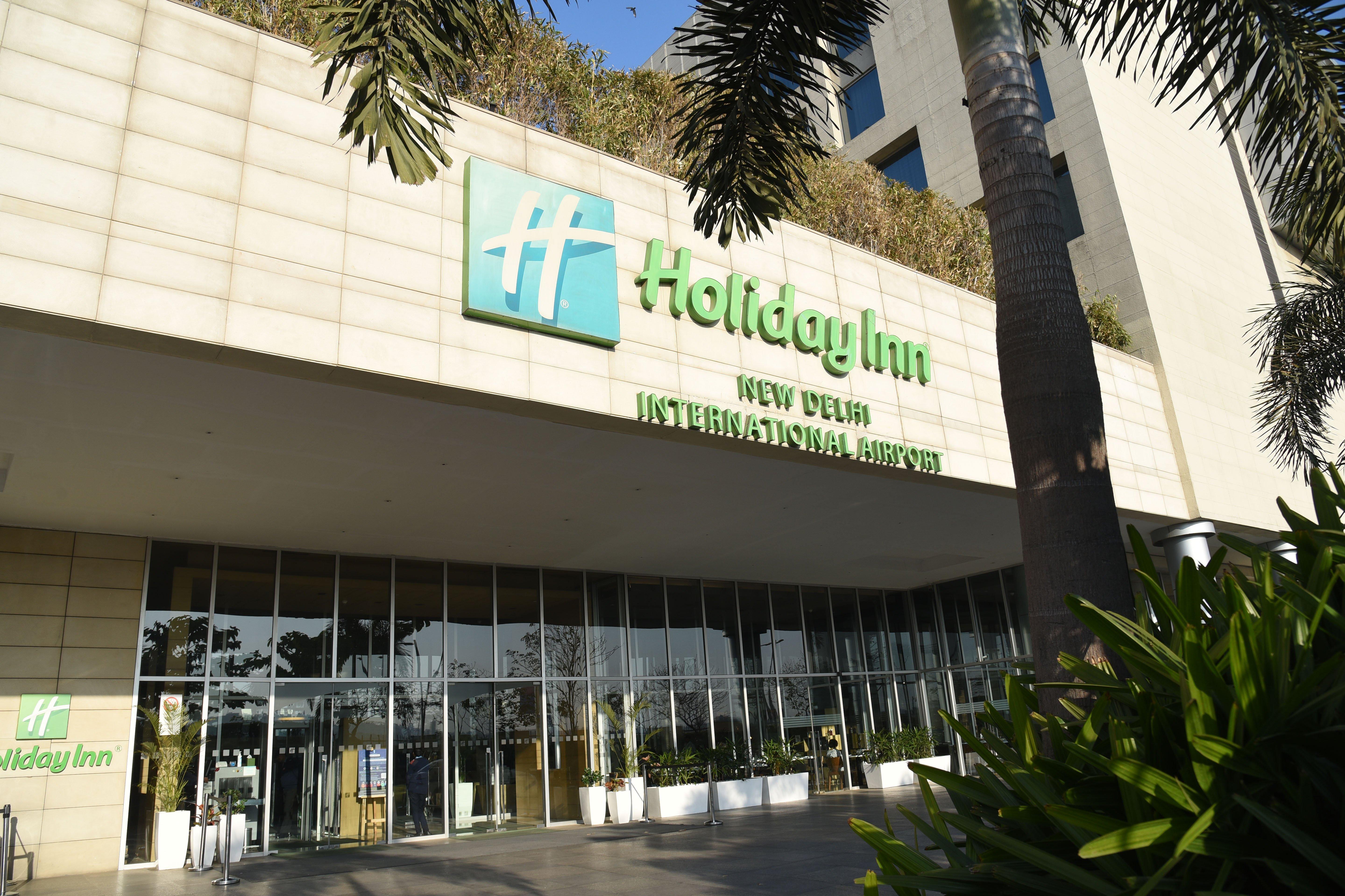 Holiday Inn New Delhi Aerocity By Ihg Exteriör bild The photo shows the exterior of a Holiday Inn hotel, specifically the Holiday Inn New Delhi International Airport. The building features a modern design with a prominent green and white sign displaying the hotel name. There are large glass doors at t